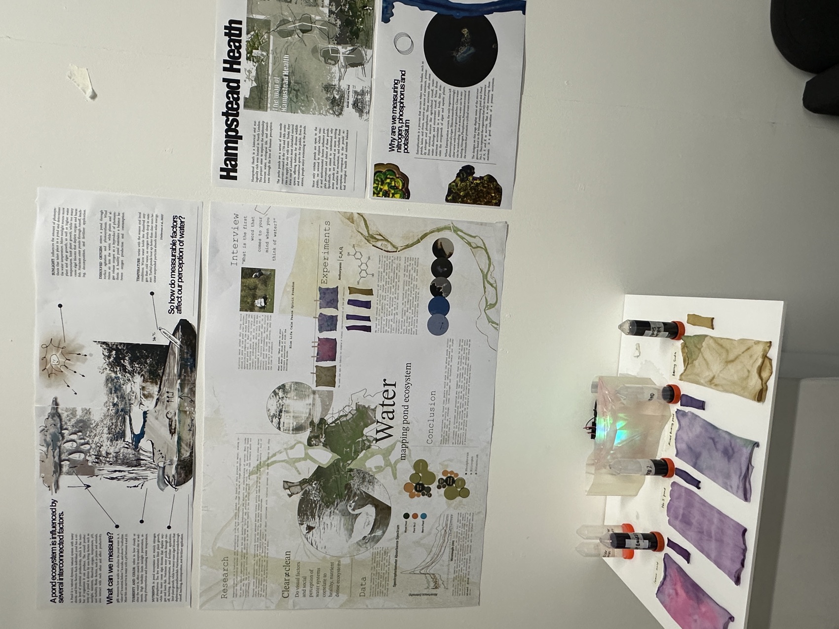 Exhibition wall with project posters, dyed fabric strips and water samples on a table